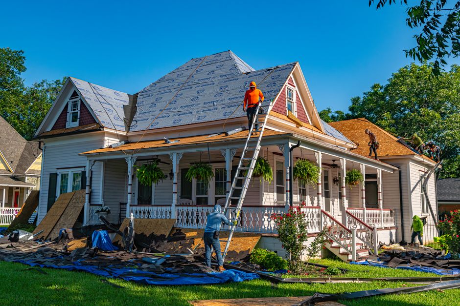Roofers at work replacing the roof covering of an older house.